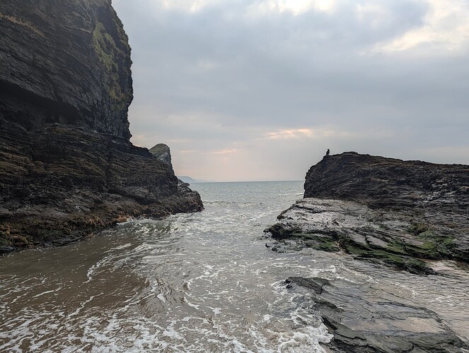 High quality image looking out to the sea with a bird on some rocks, with a cliff on the side and some cliffs in the distance