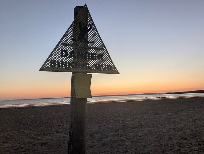 High quality image of danger sinking mud sign on the beach with the sun setting in the background