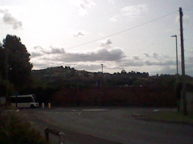 Dull picture of a bus entering a mini roundabout, with a hill behind