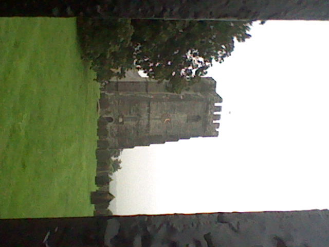 Low quality image of a church and some gravestones, with parts of a fence appearing on the side