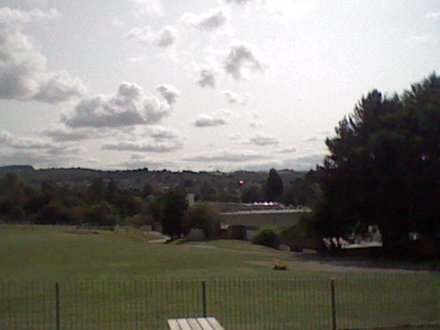 Low quality image of a fence, alongside various buildings leading up to a hill